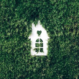 Eco house concept. Top view. White house model on green grass, forest moss background. Top view