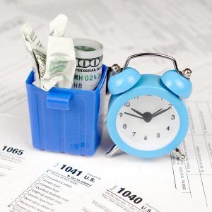 Many american tax blank forms with blue alarm clock and crumpled hundred dollar bill in trash bin